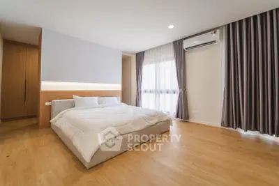 Spacious modern bedroom with wooden flooring and large windows for natural light.