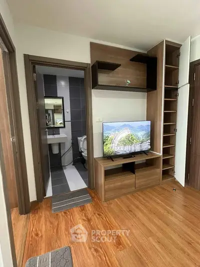Modern living room with wooden flooring and built-in TV cabinet adjacent to a bathroom.