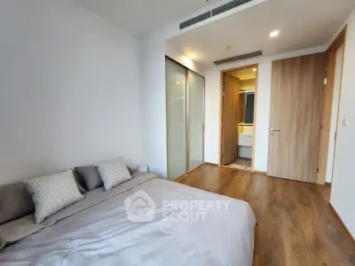 Modern bedroom with wooden flooring and ensuite bathroom in a stylish apartment.