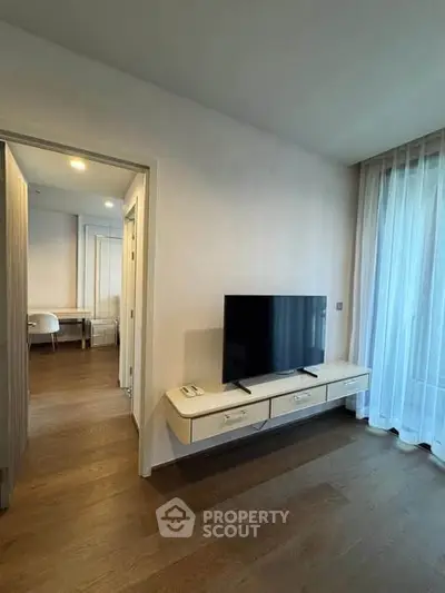 Modern living room with sleek TV stand and large window with sheer curtains.