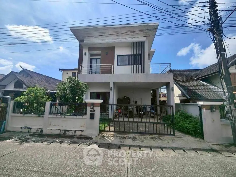 Modern two-story house with gated driveway and balcony in suburban neighborhood.