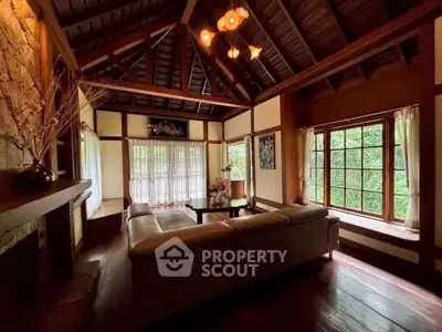 Charming rustic living room with wooden beams and large windows overlooking lush greenery.