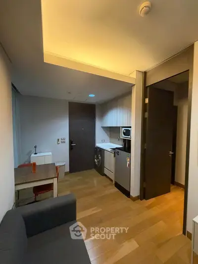 Cozy apartment interior with compact kitchen and living area, featuring modern appliances and wooden flooring.