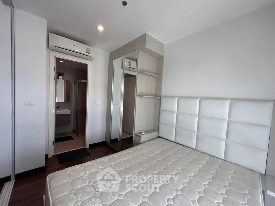 Modern bedroom with white padded headboard and mirrored wardrobe in a stylish apartment.