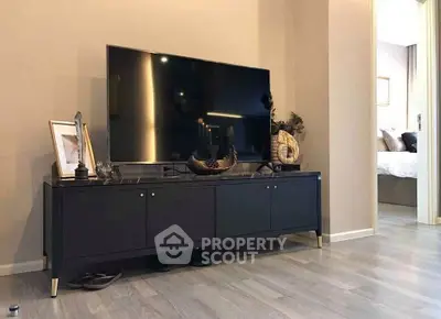 Modern living room with sleek TV stand and large flat-screen TV, showcasing stylish decor and open doorway to bedroom.