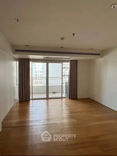 Spacious empty living room with wooden floors and balcony access in modern apartment.