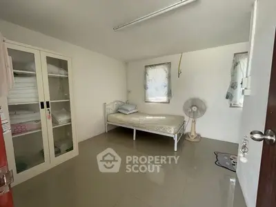 Minimalist bedroom with single bed, fan, and wardrobe in a bright, airy space.