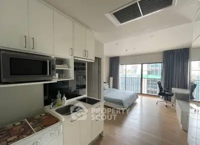 Modern studio apartment with open kitchen and cozy bedroom area, featuring a balcony with city views.