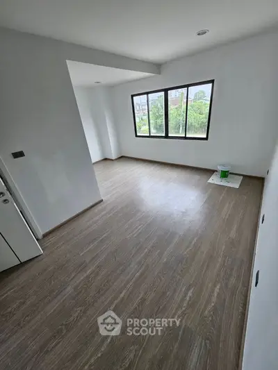 Spacious unfurnished room with large window and wood flooring, ideal for customization.