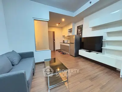 Modern living room with sleek furniture and open kitchen layout, featuring a large TV and stylish decor.