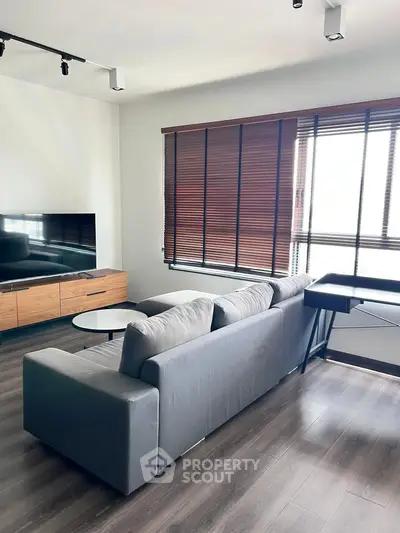 Modern living room with sleek gray sofa and large window blinds