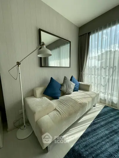 Stylish living room with modern sofa and floor lamp, featuring large window with sheer curtains.