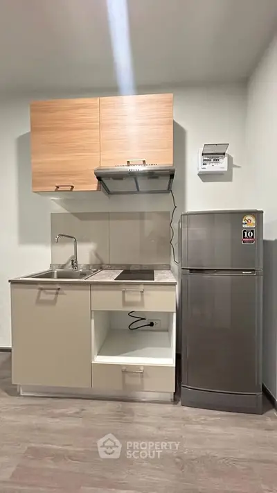 Modern compact kitchen with sleek cabinets and stainless steel fridge in a cozy apartment.