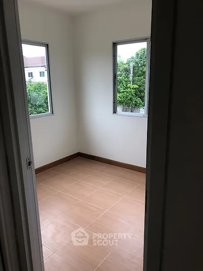 Bright empty room with tiled floor and two windows offering lush green views.