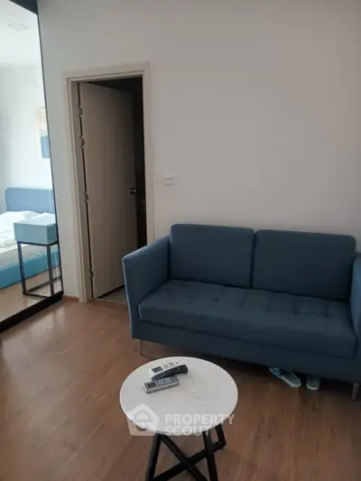 Modern living room with blue sofa and wooden flooring, adjacent to a bedroom with mirrored closet.
