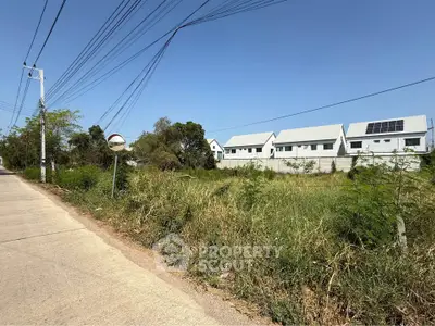 Spacious land plot with modern houses and clear blue sky, ideal for development.