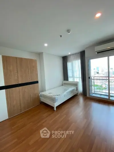 Spacious bedroom with wooden flooring and city view balcony in modern apartment.