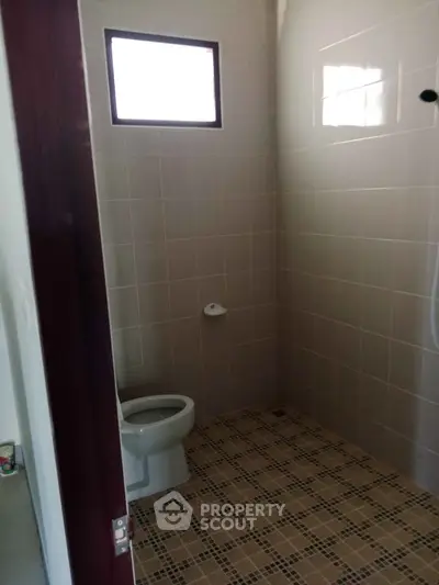 Simple bathroom with tiled walls and floor, featuring a toilet and small window.