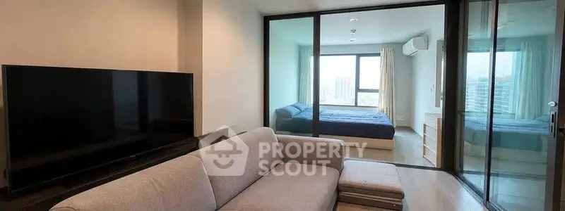 Modern living room with large TV and view into a cozy bedroom through glass doors.