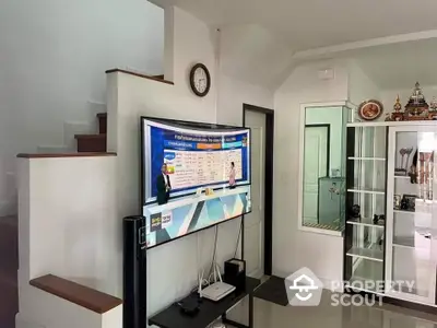 Spacious living room with modern mounted television, elegant glass cabinet, and pristine white walls complemented by a classic clock.