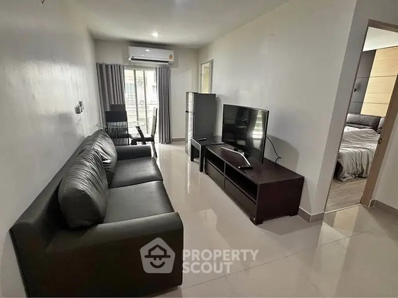 Modern living room with sleek black sofa and large TV, adjacent to a cozy bedroom.