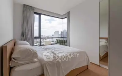 Modern bedroom with large window offering city view, featuring a cozy bed and minimalist decor.