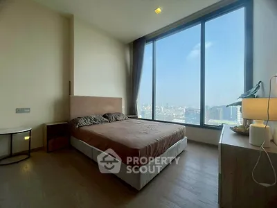 Luxurious bedroom with floor-to-ceiling windows offering stunning city views, modern furnishings, and ample natural light.