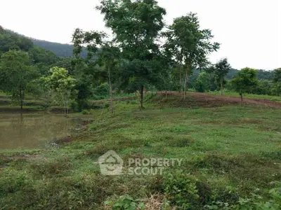 Scenic land plot with lush greenery and tranquil pond, ideal for development or agriculture.