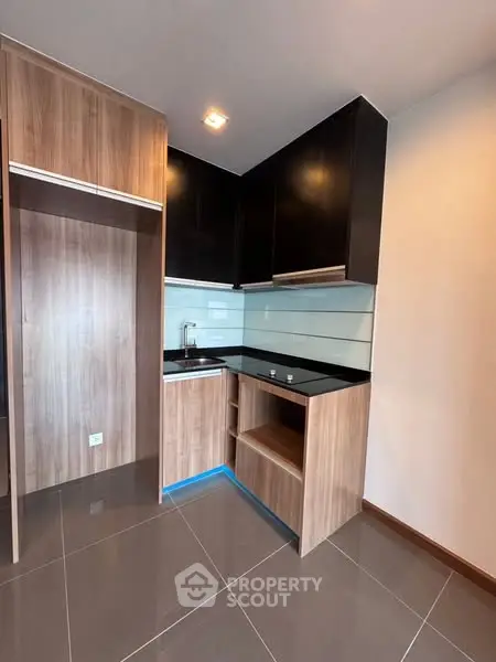 Modern kitchen with sleek black cabinets and wood accents, featuring a compact design and glossy tile flooring.