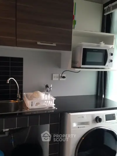 Compact kitchen with microwave and washing machine in modern apartment