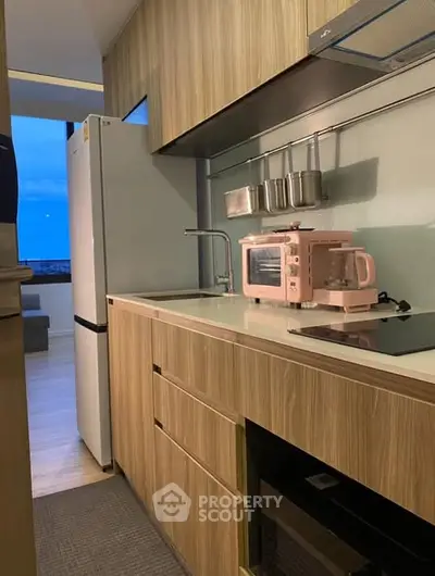 Modern kitchen with sleek wooden cabinets and pink appliances, featuring a fridge and open layout.