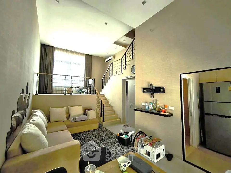 Modern living room with high ceiling and mezzanine, featuring cozy seating and stylish decor.