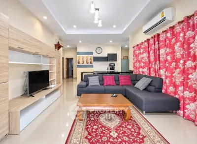 Spacious living room with modern decor, featuring a sectional sofa, wall-mounted TV, and vibrant red curtains.