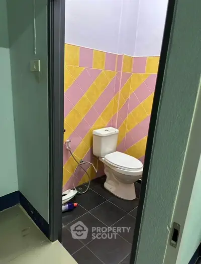 Colorful bathroom with pink and yellow tiles, featuring a toilet and tiled floor.