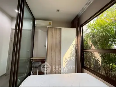 Modern bedroom with large windows and natural light, featuring a sleek wardrobe and air conditioning.