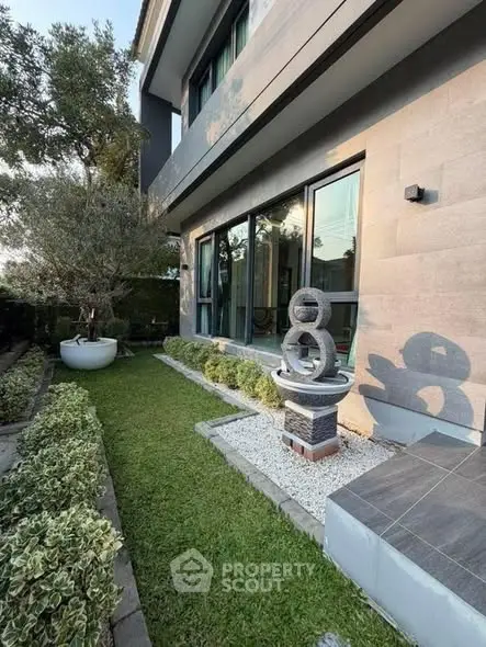 Modern house exterior with landscaped garden and unique sculpture, showcasing contemporary architecture and lush greenery.