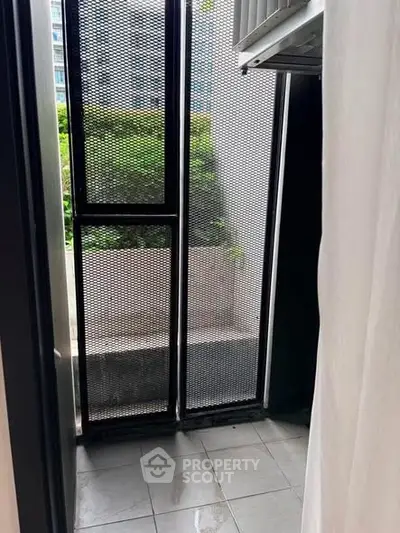 Compact balcony with metal mesh screen and garden view in modern apartment.