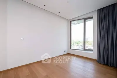 Spacious empty room with large window and wooden flooring, ideal for customization.