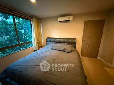 Cozy bedroom with large bed and air conditioning, featuring a window with lush greenery view.