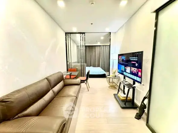 Modern living room with sleek furniture and open layout leading to a cozy bedroom.