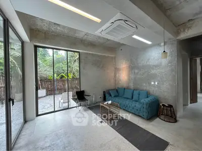 Modern living room with concrete walls and large windows overlooking a lush garden.