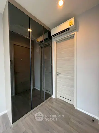 Modern bedroom with sleek mirrored wardrobe and air conditioning unit.