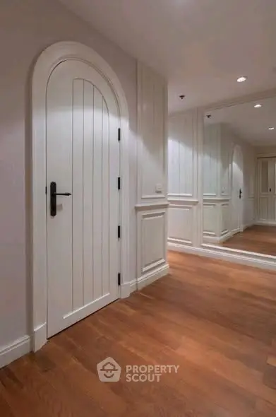 Elegant hallway with wooden flooring and arched door, featuring mirrored wall panels.