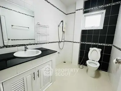 Modern bathroom with sleek black and white tiles, featuring a spacious shower and elegant vanity.