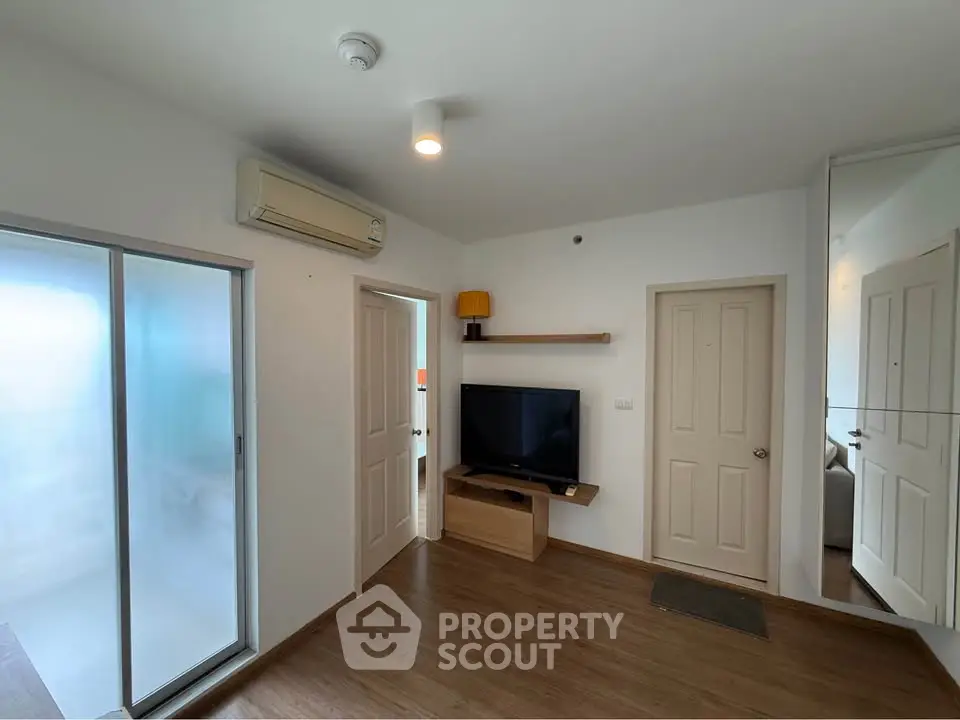 Modern living room with wooden flooring, TV setup, and air conditioning in a cozy apartment.