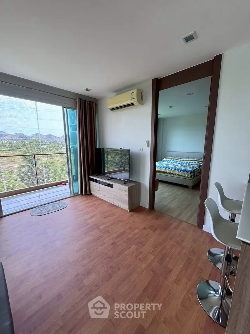 Modern living room with wooden flooring, large window, and view of bedroom in open layout apartment.