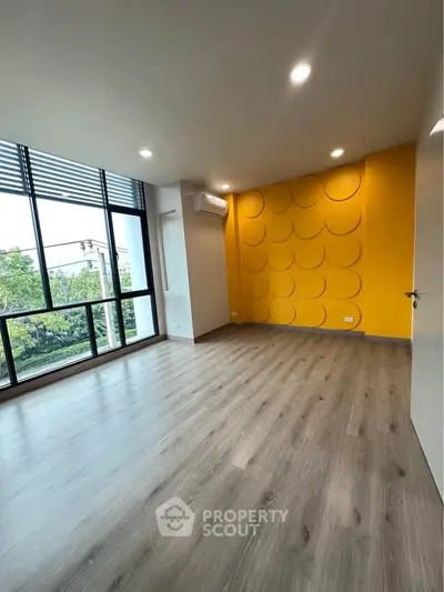 Spacious modern room with vibrant yellow accent wall and large windows offering natural light.