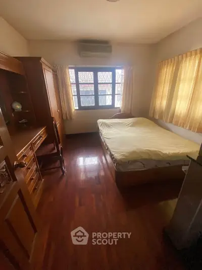 Cozy bedroom with wooden flooring and ample natural light from large window.