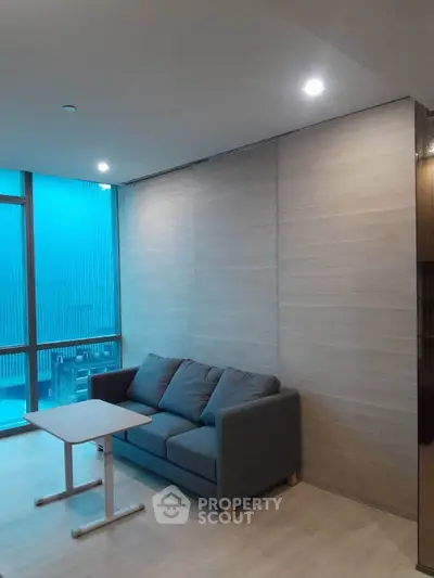 Modern living room with cozy sofa and sleek table, featuring large windows for natural light.