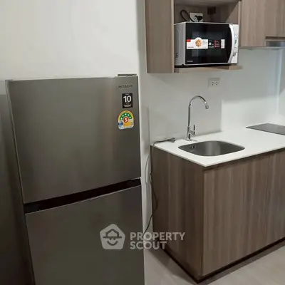 Modern kitchen with stainless steel fridge and microwave, sleek cabinetry, and compact sink area.